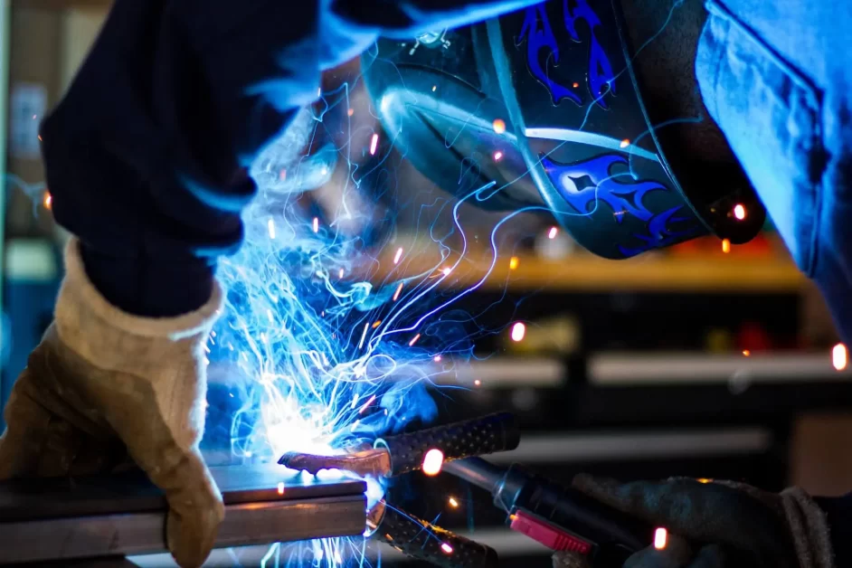 Person wearing a blue lab coat welding with sparks flying.